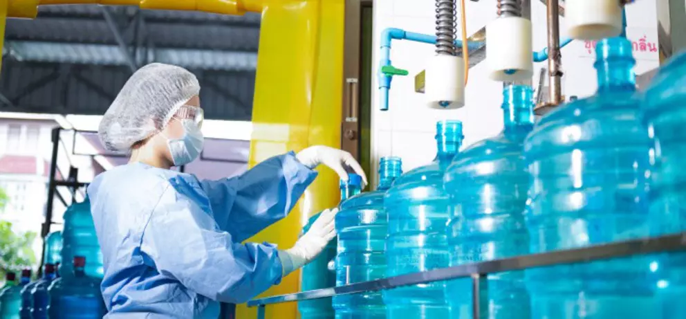 Mitarbeiter in steriler Schutzkleidung beim Handling großer Wasserflaschen in einer Industrieanlage zur Wasseraufbereitung und Abfüllung.