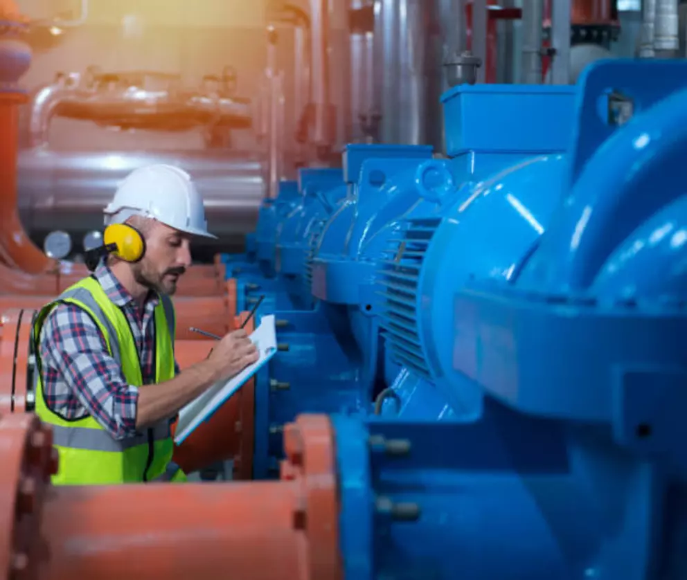 Industrieingenieur bei der Inspektion und Dokumentation von Wartungsarbeiten an großen blauen Pumpensystemen.