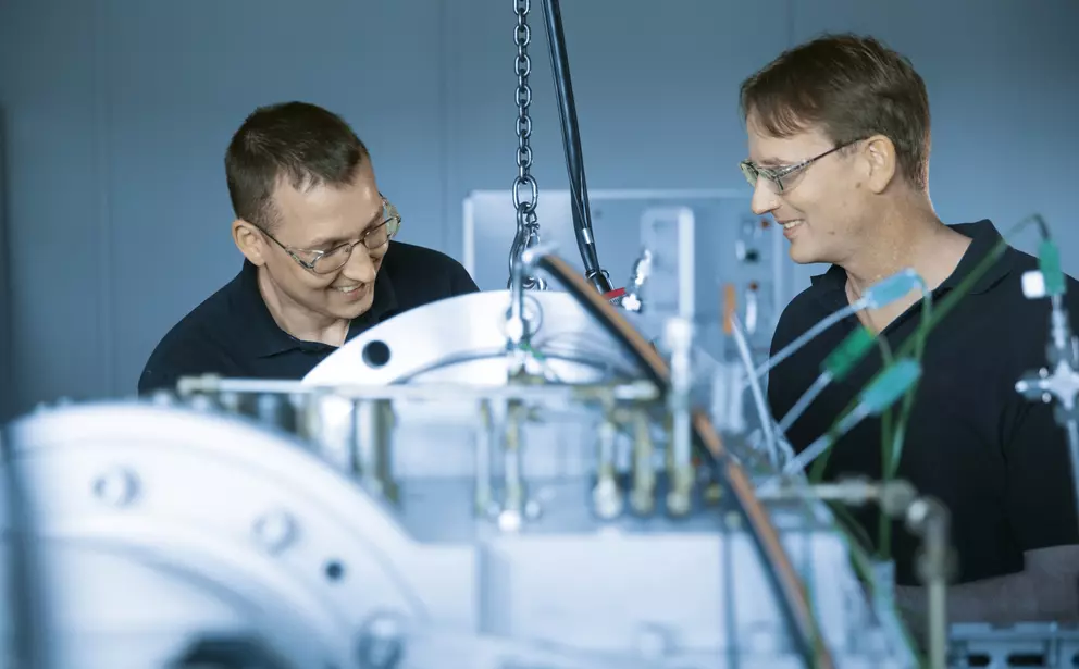 Zwei Techniker arbeiten gemeinsam an einer komplexen industriellen Prüfanlage und tauschen sich lächelnd über Mess- oder Montagearbeiten aus.