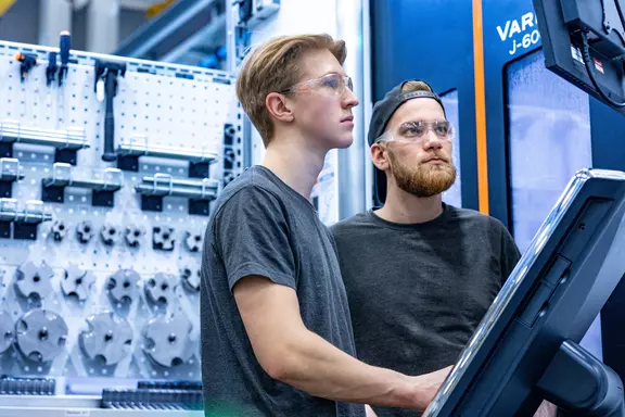 Zwei Mitarbeiter mit Schutzbrillen bedienen eine industrielle Maschine in moderner Fertigungsumgebung.