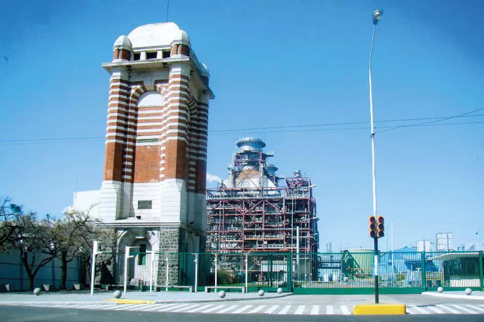 An industrial facility featuring a historic, tower A close-up of a large piece of light gray industrial machinery, showing several large hexagonal bolts secured into the casing and a smaller silver component with a sensor box attached on the right.