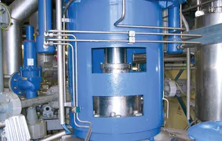 Close-up of an industrial process system with blue vessel, piping, and technical equipment.