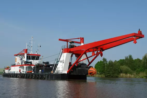 Dredging vessel with boom and cutter head operating on the water.