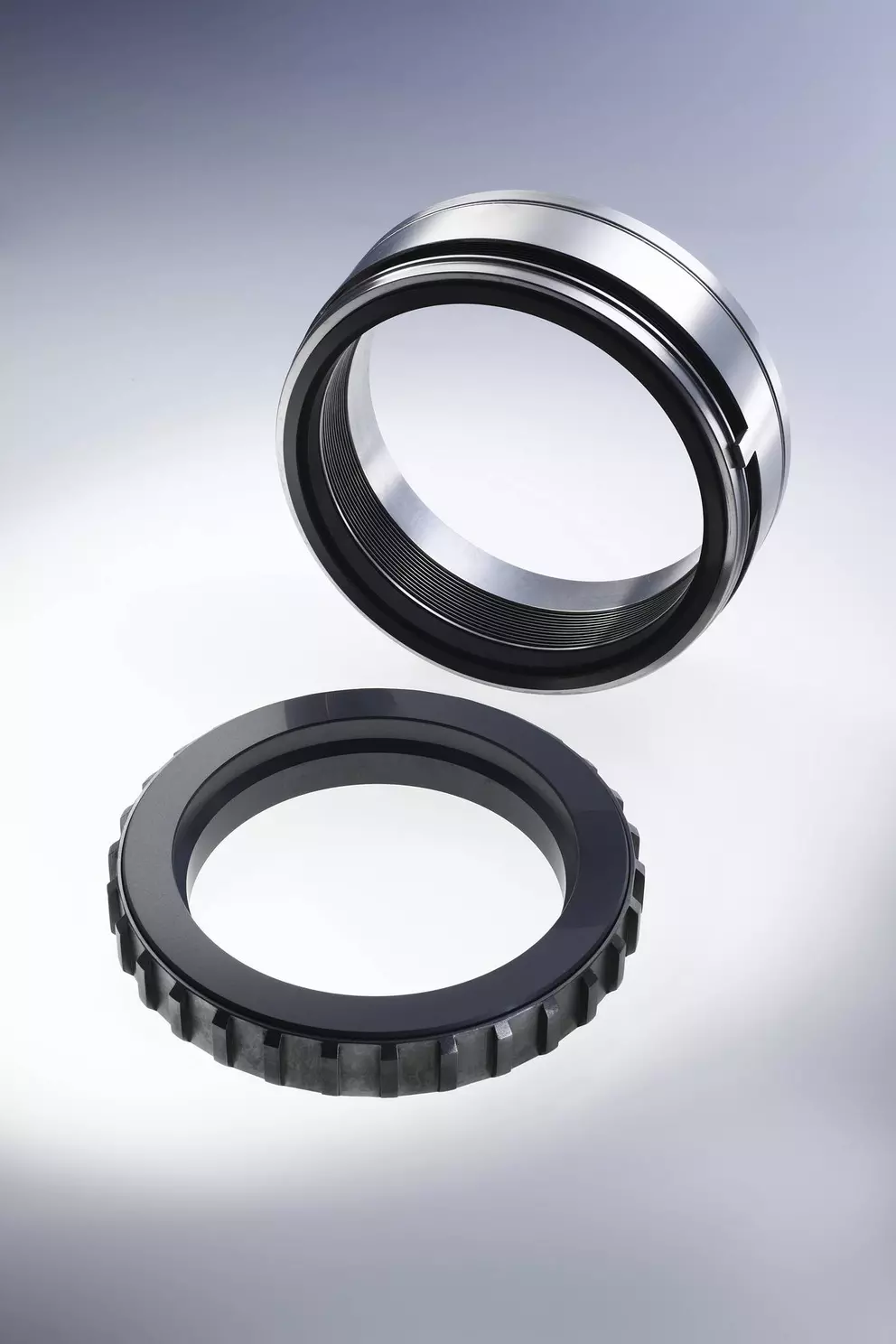 Eine Studioaufnahme von zwei kreisförmigen mechanischen Dichtungskomponenten: eine hochglanzpolierte, silberne Metallhülse, die über einem dunkleren, gezahnten Dichtungsring schwebt.