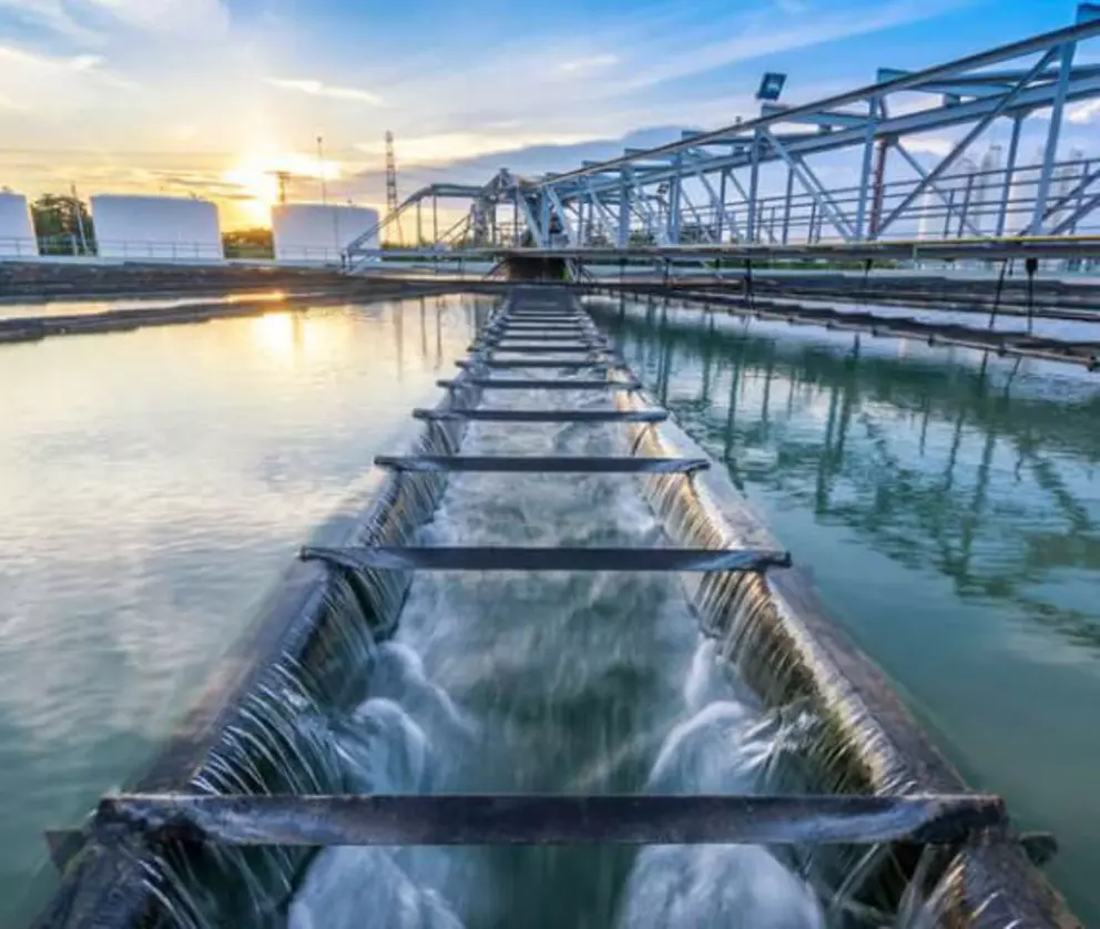 Industrial water treatment plant with sedimentation tanks and purification channels at sunset.