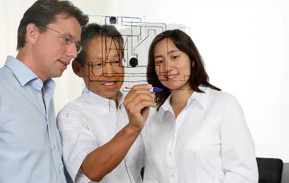 A team of engineers analyzes a technical project on a glass board during an industrial design meeting.