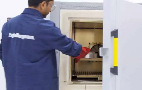 Techniker platziert ein Bauteil mit Hitzeschutzhandschuhen in einem industriellen Prüf- oder Temperofen.
