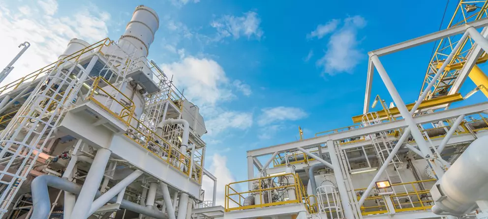 Industrielle Verarbeitungsanlage mit weißen Gebäuden und gelben Geländern vor blauem Himmel.