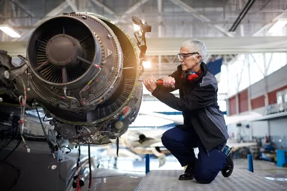 Aircraft maintenance engineer inspecting and repairing a jet engine in an aviation hangar.
