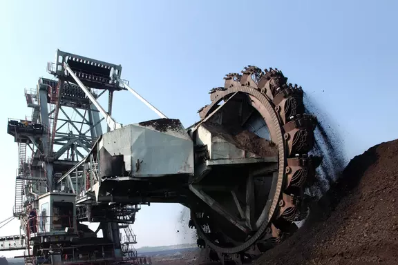 Large bucket wheel excavator mining earth in an open-pit operation under clear blue sky.