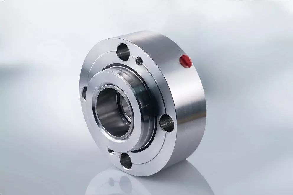 A high-angle studio shot of a clean, shiny, complex mechanical seal, likely a cartridge type, made of stainless steel with a small red indicator dot on the outer flange.